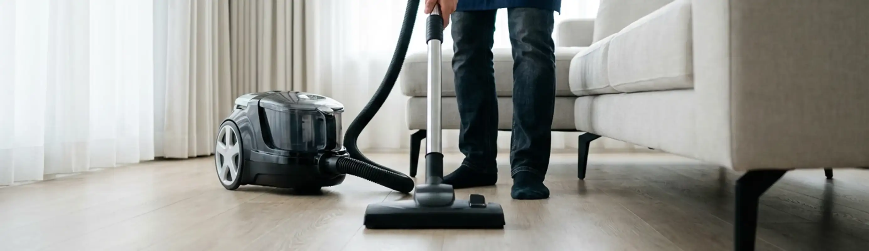 Professional house cleaner vacuuming a living room floor with a canister vacuum cleaner, Aurora, IL.
