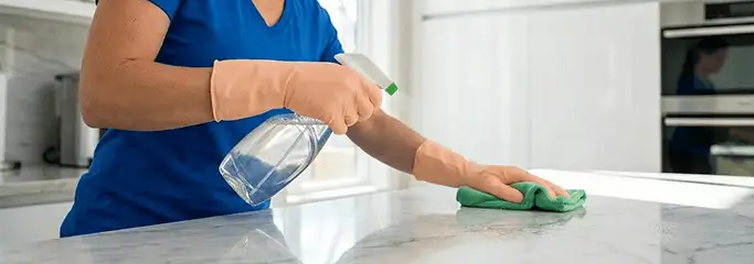Maid service worker spraying and wiping a kitchen countertop with a microfiber cloth for sanitizing, Aurora, IL.