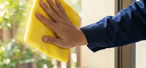 House cleaner wiping a glass window with a yellow microfiber cloth for streak-free cleaning, Aurora, IL.